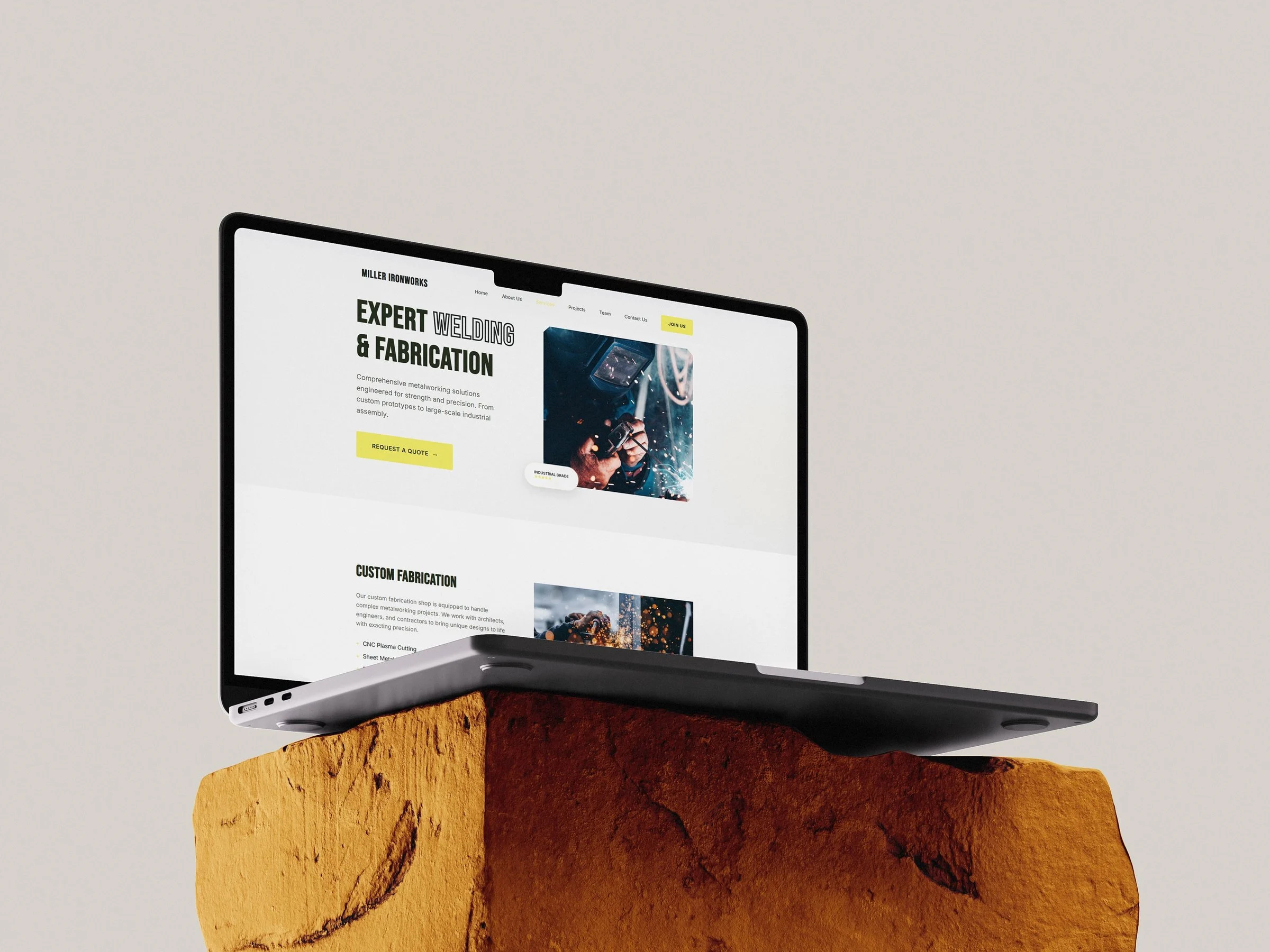 Miller Ironworks homepage on a laptop resting on a rust-colored rock, with the headline "Expert Welding & Fabrication".
